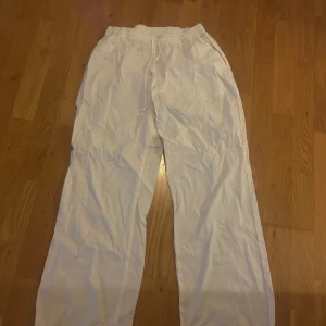 Vita byxor från Madlady - Säljer ett par vita byxor från Madlady med resår i midjan. Byxorna har en rak och lös passform och är tillverkade i ett lätt tyg, perfekta för en avslappnad stil. Storlek M/short 