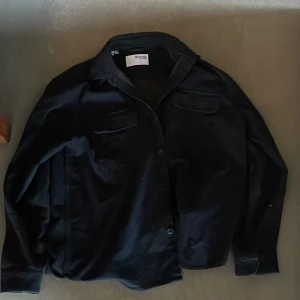 Mörk blå  overshirt från Selected Homme - Säljer en svart overshirt från Selected Homme med klassisk krage och två bröstfickor med lock. Jackan har knäppning framtill och långa ärmar. Perfekt för lager-på-lager-stil.
