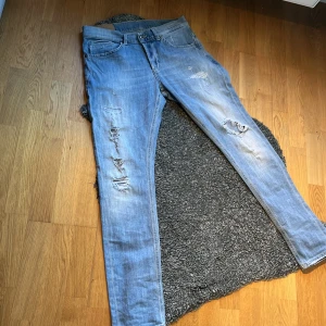 Dondup George  - Säljer ett par ljusblå jeans från Dondup med slitningar och hål på benen. Klassisk femficksmodel. Dondup logga på bakfickan. Perfekta för en avslappnad stil. Finns i dm för pris och funderingar. 