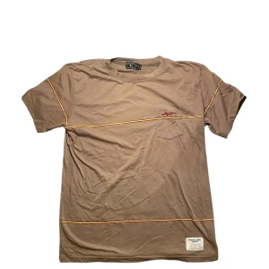 Labrador Retriever t-shirt - Säljer en brun t-shirt från Labrador Retriever med tunna gula och röda ränder tvärs över. T-shirten har en liten bröstficka och patch med 'Original Labra Vintage' nertill. Skön passform och klassisk look. Igenkligen har tröjan storlek M men passar mer som storlek S.