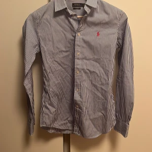Ralph Lauren Skjorta - Säljer denna snygga blå-vit randiga Ralph Lauren skjorta som är perfekt till sommaren. Skjortan är i Storlek 6 vilket motsvarar Xs. Skriv vid funderingar.