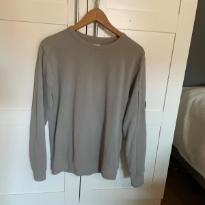 Beige långärmad tröja från C.P. Company - Tja, Säljer en stilren beige långärmad tröja från C.P. Company. Tröjan har en klassisk rund halsringning och en svart logodetalj på ena ärmen. Perfekt för dig som gillar enkel och snygg design. Kom och skriv till mig om du har några funderingar!☺️ original storlek är 14y ~ 170 men sitter som xs/s