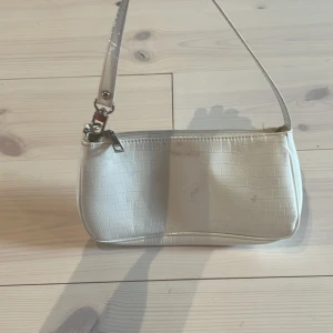 Vit axelväska med krokopräglat mönster - Säljer en stilren vit axelväska med krokopräglat mönster och silverfärgade detaljer. Den har en nån fläck vid ena sidan💓