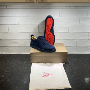 Mörkblå sneakers från Christian Louboutin - Säljer ett par mörkblå sneakers från Christian Louboutin med klassisk röd sula. Skorna är i mocka och har rund tå samt snörning. Kommer med originalkartong och dustbag. Perfekta för dig som vill sticka ut med exklusiva detaljer.