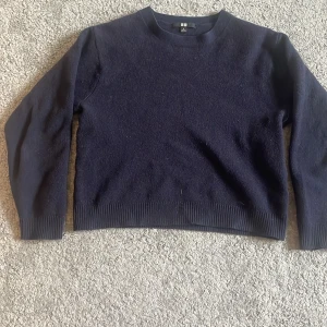 Mörkblå stickad tröja från Uniqlo - Säljer en enkel och stilren mörkblå stickad tröja från Uniqlo. Tröjan har rund halsringning, långa ärmar och ribbade muddar vid ärmslut och nederkant. Perfekt för lager-på-lager under kyliga dagar.