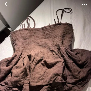 Brun babydoll topp med smock och volang - Säljer en brun babydoll med smockad överdel och volangig nederdel. Toppen har tunna axelband och är perfekt för varma dagar. Materialet känns luftigt och lätt. Finns rosetter på framsidan. Väldigt söt topp. Helt nytt skick aldrig använt, köpte i USA på american eagle