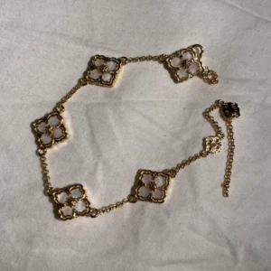Guldfärgat armband med blommiga länkar - Säljer ett elegant armband i guldfärg med flera fyrklöverformade länkar. Varje länk har en blomliknande design och armbandet har en tunn kedja med justerbar längd. Perfekt för att ge en lyxig touch till din stil. Rostar ej, i perfekt skick!