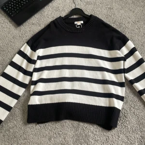 Randig stickad tröja från Gina Tricot - Säljer en svart och vit randig stickad tröja från Gina Tricot. Tröjan har långa ärmar, rund halsringning och bred ribbad kant nedtill och vid ärmsluten. Perfekt för en avslappnad och stilren look.