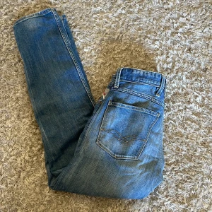 Blå Replay jeans med slitningar - Säljer ett par klassiska blå jeansbyxor från Replay med snygga slitningar och detaljer.  Modellen är anbass. L 32, midja 34 men sitter som 29 i midjan.