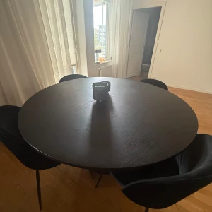 Runt matbord med svart pelarfot + stolar  - Säljer ett stilrent runt matbord i svart med en robust pelarfot och räfflad struktur. Bordsskivan är slät och har en modern design som passar perfekt i köket eller matsalen. Bordet är tillverkat i trä och har plats för flera stolar runt om. Stolarna i sammet följer med, men är köpta separat för 1000kr/st. Endast upphämtning, pris kan diskuteras. 