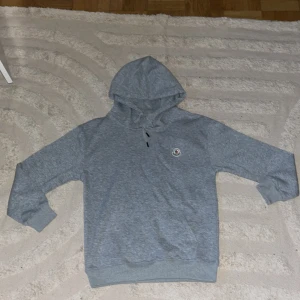 Grå hoodie från Moncler - Säljer en stilren grå hoodie från Moncler med broderad logga på bröstet. Tröjan har huva med dragsko och är tillverkad i mjuk bomull. Perfekt för en avslappnad och trendig look. Hoodien känns som storlek s. Så om du har storlek s på kläder så kommer denna passa perfekt.
