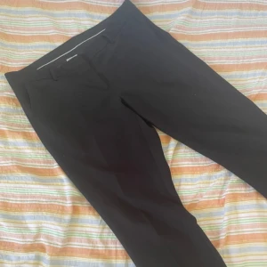 Svarta kostymbyxor från KappAhl Kelly - Säljer ett par svarta kostymbyxor från KappAhl, modell Kelly. Byxorna har klassisk passform med avsmalnande ben och diskreta fickor både fram och bak. Perfekta för en stilren och enkel look.