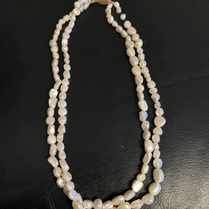 Vitt pärlhalsband med gulddetalj - Elegant halsband med vita pärlor i två rader och en dekorativ guldfärgad låsdetalj. Perfekt för att ge en klassisk touch till din outfit.