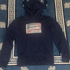 Mörkblå hoodie från Ralph Lauren - Säljer en snygg mörkblå hoodie från Ralph Lauren med ett tryck av en amerikansk flagga på bröstet. Perfekt för en avslappnad stil. Hör av dig vid fler frågor!