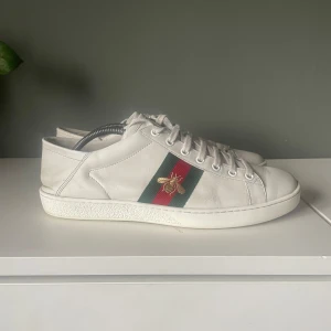 Gucci ace bees soft - Snygga vita sneakers med gröna och röda ränder samt en guldfärgad bi-detalj på sidan. Skorna har snörning och en klassisk design som passar perfekt för en stilren look. Går runt 3999kr men säljer de för 1500kr. Perfekta till sommarn. 