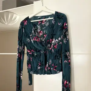 Snygg blommig omlottopp i grönt med rosa och vita blommor. Hör av er vid funderingar eller om ni vill ha bilder med hur plagget sitter på mig. Titta gärna in mina andra plagg!