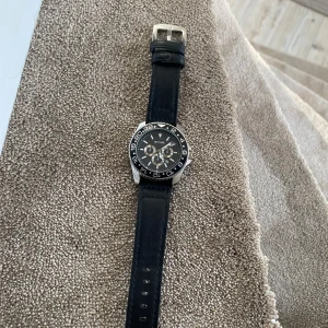 Svart klocka från Skyline - Snygg Skyline-klocka med svart urtavla och silverdetaljer. Den har en svart läderrem och en boett i rostfritt stål. Perfekt för dig som gillar en stilren look.