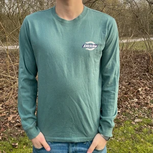 Grön långärmad tröja från Dickies - Säljer en grön långärmad tröja från Dickies med logga på bröstet och ryggen. Perfekt för en avslappnad stil. Tröjan har en rund halsringning och är gjord i ett mjukt material. Modellen är 180