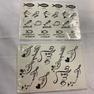 Svarta temporära tatueringar med text och symboler - Två ark med svarta temporära tatueringar. Det ena arket har religiösa symboler som fiskar och ordet 'Jesus'. Det andra arket innehåller ord som 'Love' och dekorativa hjärtan och stjärnor. Perfekt för att uttrycka stil och känsla.