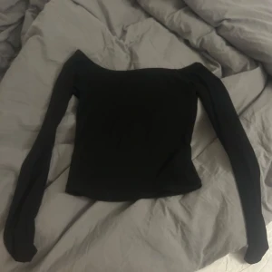 Svart offshoulder topp från Gina Tricot - Snygg svart offshoulder topp från Gina Tricot. Perfekt för en stilren look med långa ärmar och en tight passform. Enkelt att matcha med olika outfits. Storlek S, aldrig använd. Säljer då den är för liten!