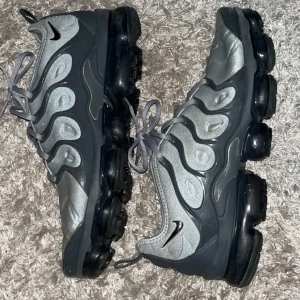 Nike Air Vapormax Plus i grått och svart - Snygga Nike Air Vapormax Plus sneakers i en stilren grå och svart färgkombination. Skorna har en unik bubbelsula och snörning för en bekväm passform. Perfekta för både träning och vardagsbruk. Strl 45 gott skick inga skador eller liknande nypris ca 3000