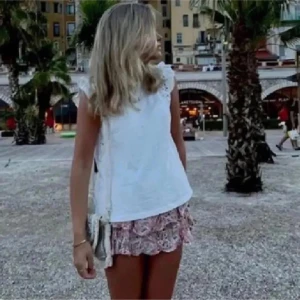 Mönstrad rosa kjol från Zara - Säljer en söt och somrig rosa kjol från Zara med ett vackert blommönster i vitt och beige. Kjolen har en volangdetalj som ger den en extra charmig look. Perfekt för varma dagar! Den har inbyggda shorts! (första bilden är lånad)