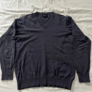 Grå tröja från Peak Performance - Säljer en stilren mörkblå tröja från Peak Performance med v-ringning. Tröjan har långa ärmar och ribbade muddar vid ärmslut och nederkant. Perfekt för en avslappnad och snygg look. Den är i storlek L men passar även M. Den är i bra skick