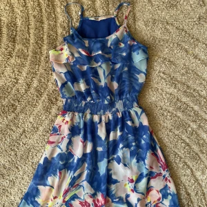 Blommig klänning från H&M - Säljer en färgglad blommig klänning från H&M i blått och rosa. Klänningen har smala axelband och ett elastiskt midjeband för en bekväm passform. Perfekt för sommarens varma dagar! 🌸