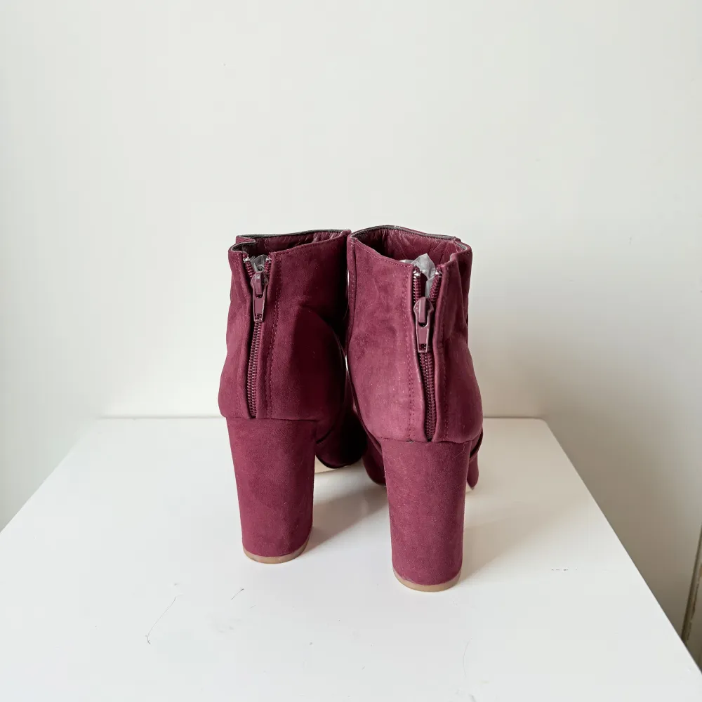 Snygga vinröda boots i mocka med en stabil klack och dragkedja baktill. Perfekta för att ge en färgklick till din outfit. De har en spetsig tå och är idealiska för höst och vinter. Använt skick, tecken finns. Svårt att få på bild. Storlek 38.. Kengät.