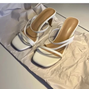 Vita klackskor - Eleganta vita sandaler med klack och smala remmar. De har en fyrkantig tå och en stilren design som passar perfekt för sommarens tillfällen. (SÄLJER PGA FÖR SMÅ)