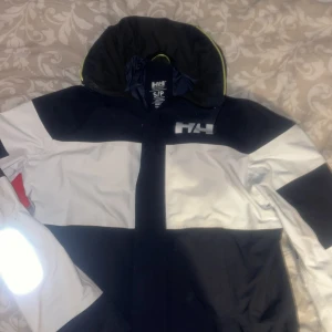 Seglarjacka från helly hansen  - Säljer en svart o vit seglarjacka från Helly Hansen. Dragkedja med resår och två framfickor och reflexdetaljer. Liten svart fläck bak vid högra ärmen som jag inte lyckats få bort men annars i toppen skick.