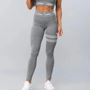 Grå träningsbyxor Stronger - Snygga grå träningsbyxor från Stronger med hög midja och elastisk linning. De har två vita ränder runt låret. Perfekta för träning eller en aktiv vardag. Finns inte att köpa på strongers hemsida🩶