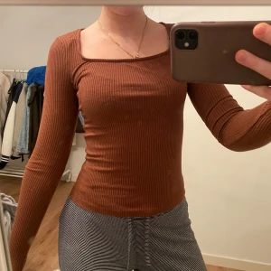 Brun ribbad topp - Säljer en snygg brun ribbad topp med lång ärm. Perfekt för en stilren look. Toppen har en tight passform och är gjord i ett mjukt material. Den är köpt på Na-Kd och är knappast använd.