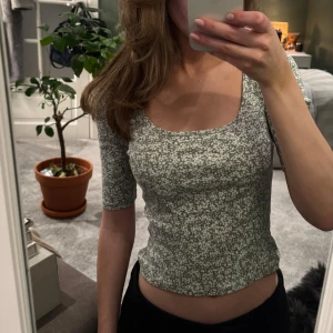 Grön blommig topp från Lindex  - Säljer en söt grön topp med blommigt mönster från Lindex. Toppen har en fyrkantig urringning och trekvartsärmar, perfekt för vår och sommar. Den är figurnära och passar bra till både jeans och kjol. 🌸