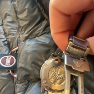 Silverfärgad klocka från Emporio Armani - Snygg silverfärgad klocka från Emporio Armani med en stilren design. Klockan har en metallarmband och en mörk urtavla med tydliga markeringar. Perfekt för den som gillar en klassisk och elegant stil.