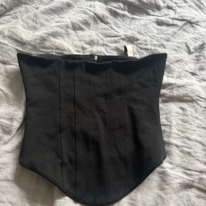 Svart korsett med dragkedja - Snygg svart korsett med dragkedja i ryggen. Perfekt för att ge en stilren och elegant look. Passar bra till olika outfits och tillfällen.