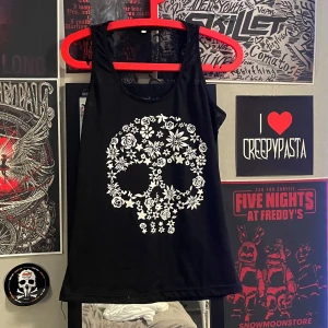 Svart linne med dödskalle - Snyggt svart linne med ett coolt vitt dödskallemotiv av blommor på framsidan. Baksidan har en transparent spetsdetalj