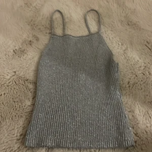Glittrig silverfärgad linnetopp från H&M - Säljer en snygg glittrig silverfärgad linnetopp från H&M. Toppen har smala axelband och en ribbad struktur som ger en stilren look. Perfekt för att lysa upp vilken outfit som helst! ✨