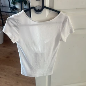 Vit kortärmad topp med knyt - Säljer en vit kortärmad topp med knyt framtill. Toppen har en enkel och stilren design med en rund halsringning och är perfekt för en avslappnad look.