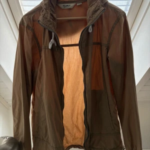 Beige vindjacka från Pull&Bear - Säljer en beige vindjacka från Pull&Bear med dragkedja och huva. Jackan har långa ärmar och justerbara snören vid huvan. Perfekt för blåsiga dagar! NÅGOT MINDRE I STROLKEN skulle påstå att den motsvarar M