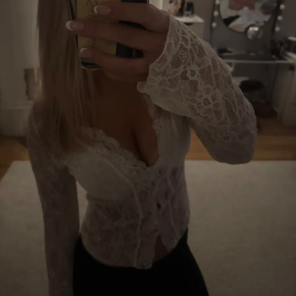 Säljer en elegant vit spetsblus med långa ärmar och v-ringad design. Blusen har knappar framtill och ett vackert spetsmönster som ger en romantisk känsla. Perfekt för att klä upp en outfit eller för speciella tillfällen.. Yläosat.