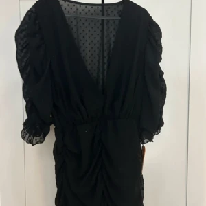 Svart klänning med prickigt mönster - Elegant svart klänning med v-ringning och prickigt mönster. Klänningen har volangdetaljer och trekvartsärmar, vilket ger en romantisk touch. Perfekt för en kväll ute eller en speciell tillställning.