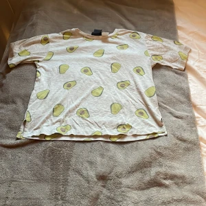 Vit t-shirt med avokadotryck - Säljer en cool vit t-shirt med avokadotryck. Perfekt för en avslappnad stil med en rolig twist. T-shirten har korta ärmar och en normal passform. Perfekt för sommardagar eller som en rolig detalj i garderoben! 🥑