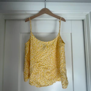 Gul blommig linnetopp från H&M - Säljer en söt gul linnetopp från H&M med vita blommor. Toppen har smala axelband och en luftig passform, perfekt för varma sommardagar, eller som pyjamas!💓