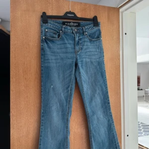 Blå jeans från John Richmond - Snygga blå jeans från John Richmond med bootcut-stil. De har en klassisk femficksdesign och en knappgylf. Perfekta för en avslappnad look.