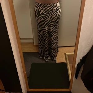 Zebramönstrad långkjol - Snygg zebramönstrad långkjol i svart och beige. Kjolen har en tight passform som framhäver figuren och är perfekt för en trendig look. Materialet ser ut att vara mjukt och följsamt, vilket ger en bekväm känsla. Den är ifrån New yorker och säljer för 300