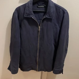 Mörkblå jacka från J.Lindeberg - Snygg mörkblå jacka från J.Lindeberg med dragkedja framtill. Jackan har en klassisk krage och långa ärmar. Perfekt för en stilren look.