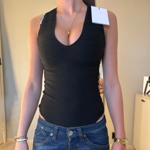 Svart ribbad linnetopp - Snygg svart ribbad body med djup v-ringning. Perfekt för en stilren look