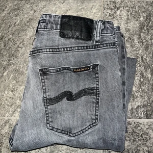 Grå Nudie Jeans - Jättesnygga grå Nudie jeans med fet tvätt säljes. De har en ganska slimmad och rak passform. Enda defekten är ett litet hål i höger ficka, annars är dem riktigt fina. Storlek 28/30
