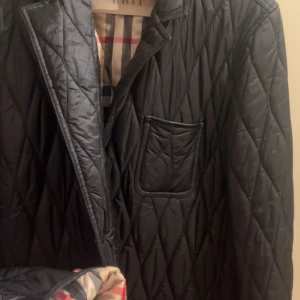 Svart quiltad jacka från Burberry Brit - Burberry Quilted Jacket – Size L (Fits Like M)  Selling an authentic Burberry quilted jacket, size L but fits more like a Medium. Worn only once or twice – excellent condition with no defects. Classic design with the iconic Burberry check lining. 100% genuine – original price: 6999 SEK. A great opportunity to get a luxury piece at a better price!